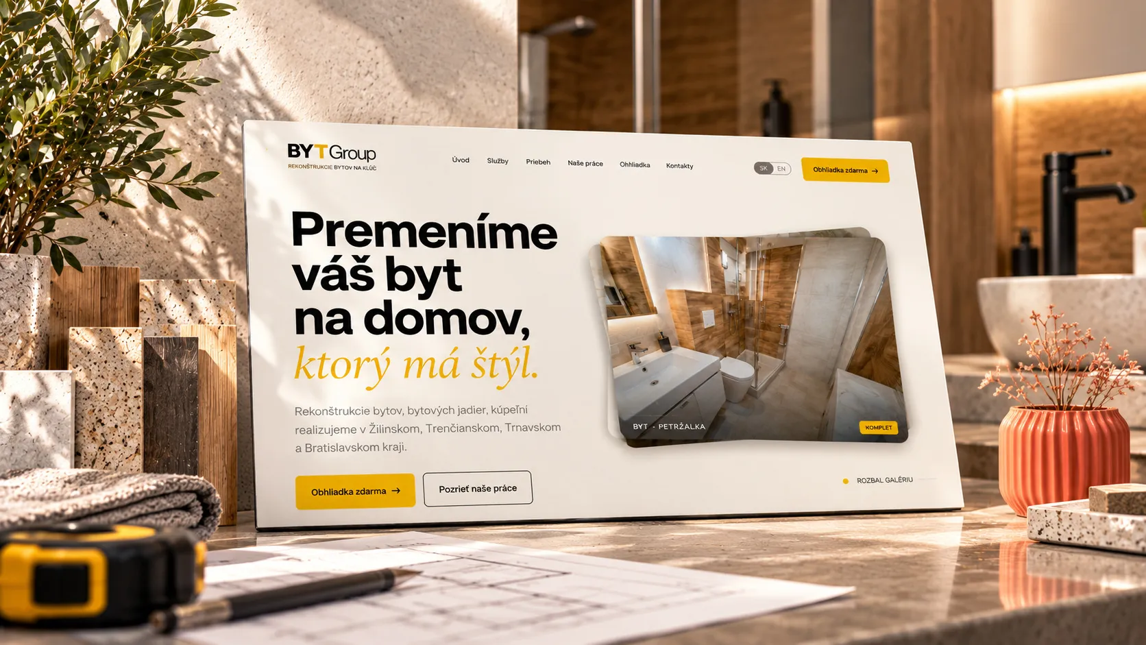 The BYTGroup website home page on a screen among stone and wood samples, a tape measure, a drawing and a coral vase.