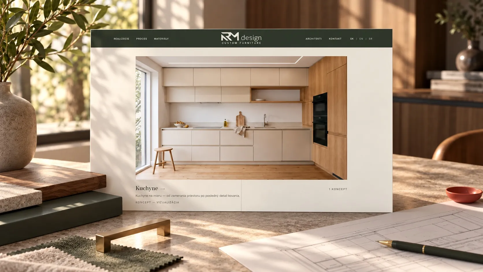 The RM design website on a screen on a work desk: the “Kuchyne” category with a kitchen visualization labelled “koncept — vizualizácia”. Beside it material samples, a brass handle and drawings with a pen.