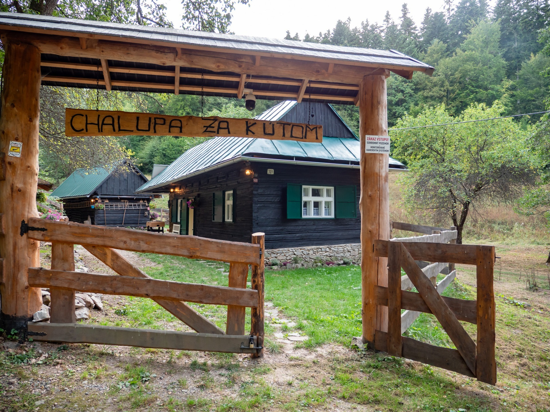 The entrance to Chalupa Za Kútom with a wooden gate and the cottage in the forest